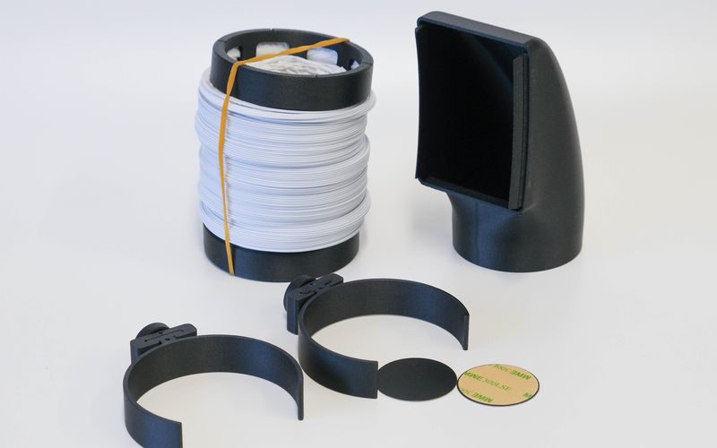 Gedruckte Prototyp-Teile in Schwarz: zwei Schlauchhalter, Ringe und ein Lüftungsstutzen auf weißem Grund